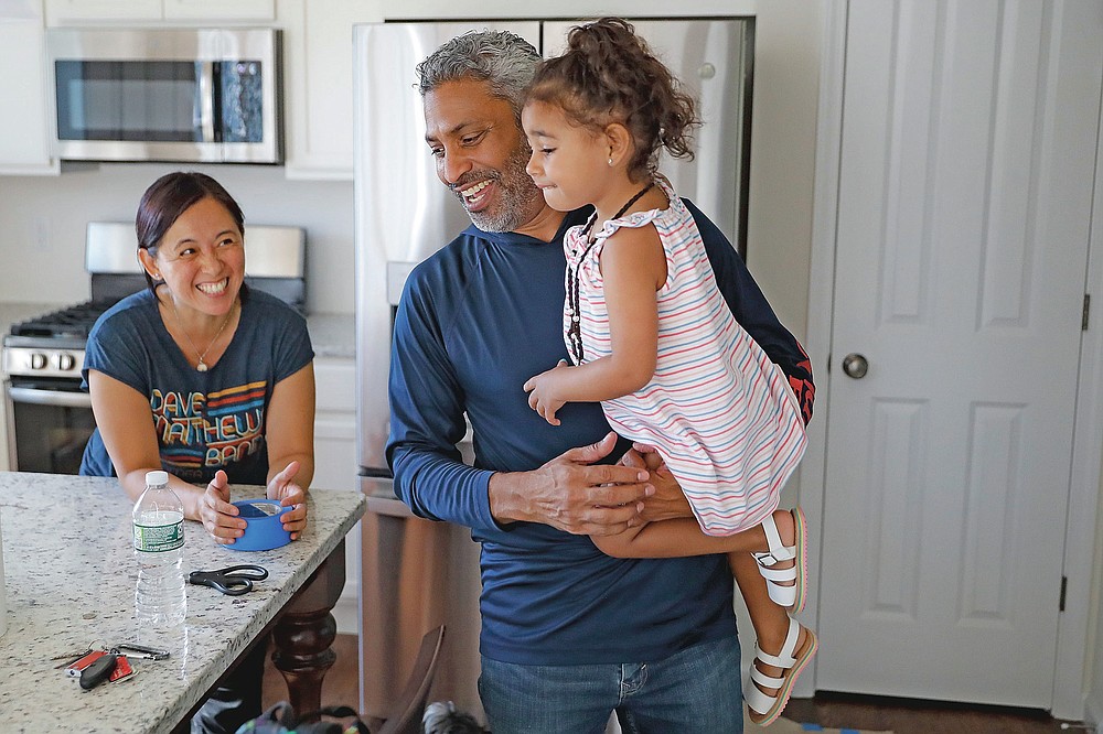 Anil Lilly, center, holds his granddaughter Paige alongside his wife, Joyce, at their new home, Tuesday, July 21, 2020, in Washingtonville, N.Y. New Yorkers anxious after weathering the worst of the coronavirus pandemic are fueling a boom in home sales and rentals around the picturesque towns and wooded hills to the north. Real estate brokers and agents describe a red-hot market recently, with many house hunters able to work from home. (AP Photo/John Minchillo)