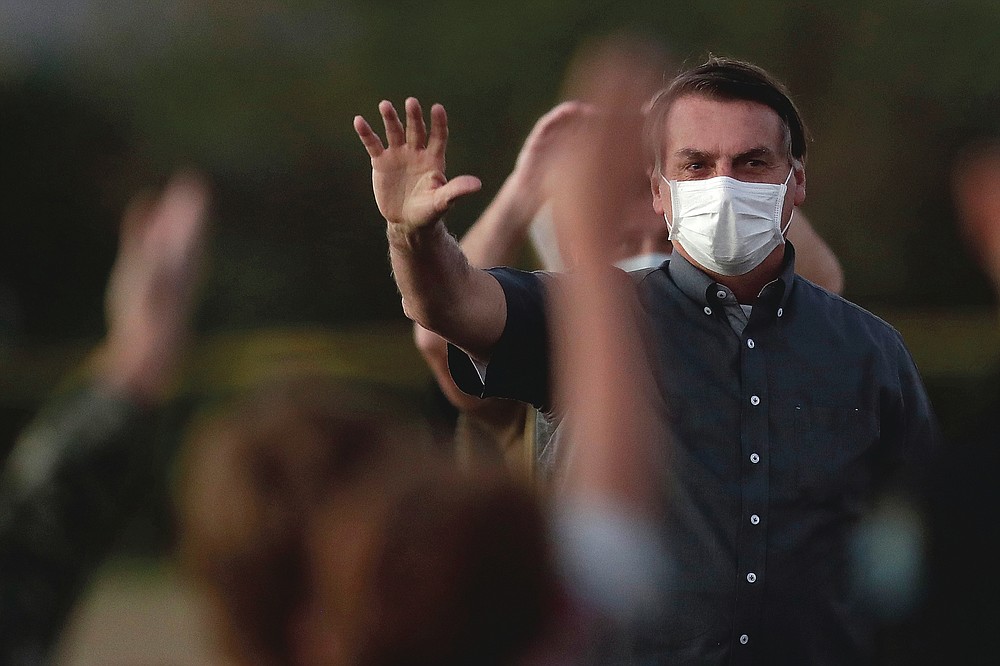 FILE - Brazil's President Jair Bolsonaro, who is infected with COVID-19, wears a protective face mask as he waves to supporters during a Brazilian flag retreat ceremony outside his official residence in Brasilia, Brazil on July 20, 2020. The countries which top the rankings of COVID-19 deaths globally are led by populist, mold-breaking leaders like Bolsonaro. The U.S., Brazil, the United Kingdom and Mexico all are led by leaders who have been skeptical of the scientists and who initially minimized the disease. And their four countries alone account for half of the total 585,000 COVID-19 deaths worldwide so far, according to statistics tracked by Johns Hopkins University. (AP Photo/Eraldo Peres, File)