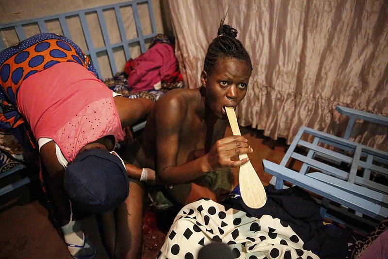 Veronica Atieno, center, bites down on a wooden cooking spoon as traditional birth attendant Emily Owino, left, assists her before delivering her baby in Emily's one-room house during a dusk-to-dawn curfew, in the Kibera slum of Nairobi, Kenya in the early hours of Friday, May 29, 2020. Kenya already had one of the worst maternal mortality rates in the world, and though data are not yet available on the effects of the curfew aimed at curbing the spread of the coronavirus, experts believe the number of women and babies who die in childbirth has increased significantly since it was imposed mid-March. (AP Photo/Brian Inganga)