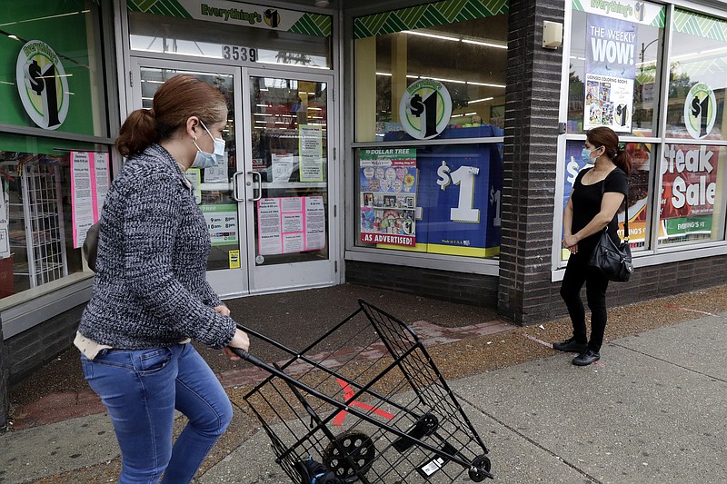 FILE - In this Friday, May 15, 2020, file photo, a woman wearing a mask, left, walks by a Dollar Tree, while another woman waits in line to shop at the store, which is limiting customers amid the coronavirus pandemic, in Chicago. (AP Photo/Nam Y. Huh, File)