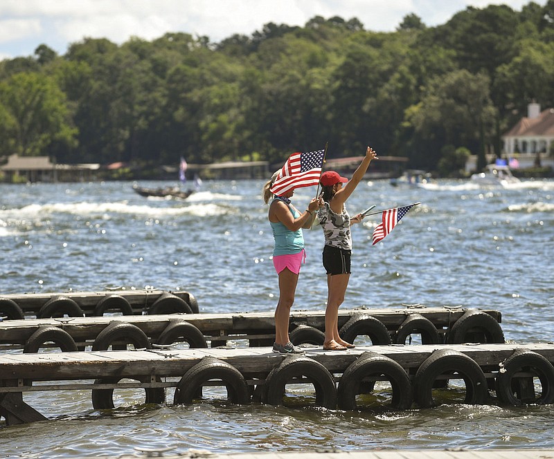 Two unidentified women wave to a crowd of passing boats on Lake Hamilton Sunday morning as the Trump Pence Keep America Great 2020 Boat Parade passes by. - Photo by Grace Brown of The Sentinel-Record