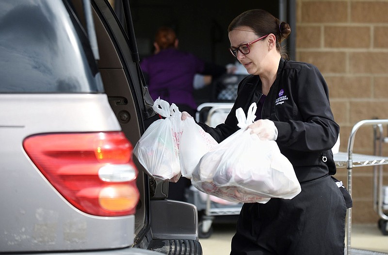 Shonda Holt, kitchen manager at Happy Hollow Elementary School, places bags of meals Tuesday in cars at Owl Creek School in Fayetteville. Ten meal pick-up began Tuesday with the school distributing five breakfasts and five lunches for any child age 18 and younger. More information is available at https://bit.ly/2UyVFrg. Visit nwaonline.com/200401Daily/ and nwadg.com/photos for a photo gallery.
(NWA Democrat-Gazette/David Gottschalk)