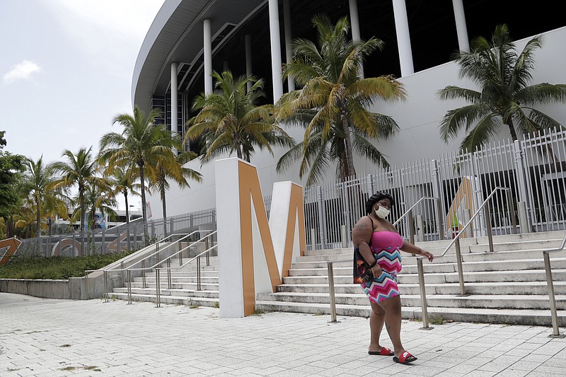 A woman wearing a protective face covering walks past Marlins Park, Monday, July 27, 2020, in Miami. The Marlins home opener against the Baltimore Orioles on Monday night has been postponed as the Marlins deal with a coronavirus outbreak that stranded them in Philadelphia. (AP Photo/Lynne Sladky) story.lead_photo.caption