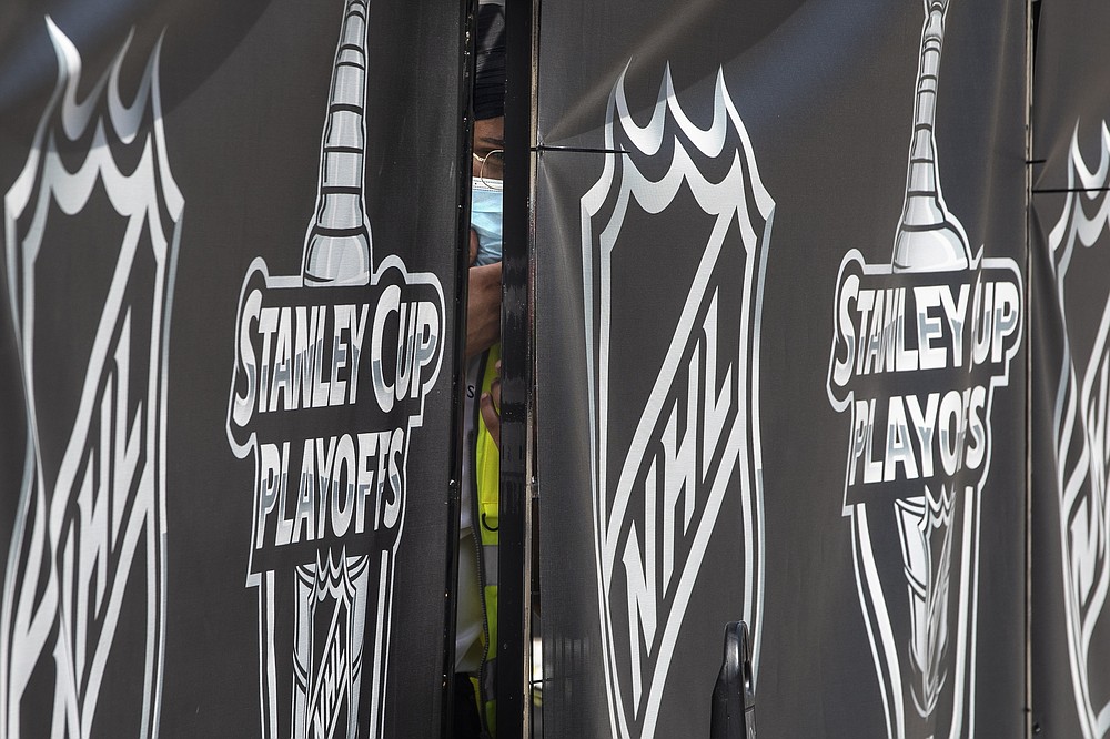 A security guard peers out from behind NHL-branded fencing at the entrance where players arrive at Toronto's Royal York hotel, which is acting as the "bubble" ahead of the return of the league's season following disruption due to the COVID-19 pandemic, Sunday, July 26, 2020. (Chris Young/The Canadian Press via AP)