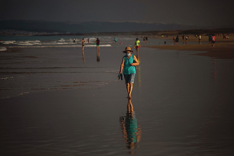 A woman wearing a face mask walks at the beach in Zahara de los Atunes, Cadiz province, south of Spain, on Saturday, July 25, 2020. Ministers are set to remove Spain from the Government's list of safe countries to travel to after the European country saw a rise in Covid-19 cases. The decision means those coming back from Spain will have to self-isolate for two weeks upon their return to England. (AP Photo/Emilio Morenatti)