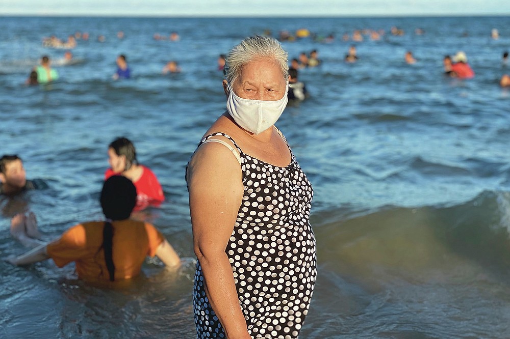 A woman wearing a face mask stands on a beach in Vung Tau city, Vietnam, Sunday, July 26, 2020. Vietnam on Sunday reimposed restrictions in one of its most popular beach destinations after a second person tested positive for the virus, the first locally transmitted cases in the country in over three months. (AP Photo/Hau Dinh)