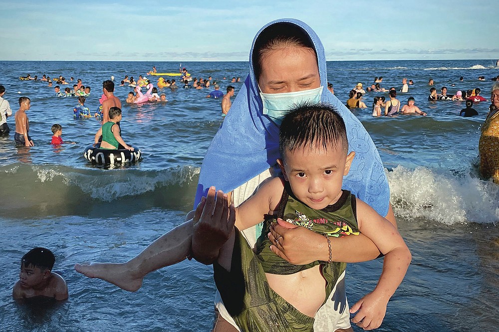A woman wearing a mask carries her child on a beach in Vung Tau city, Vietnam, Sunday, July 26, 2020. Vietnam on Sunday reimposed restrictions in one of its most popular beach destinations after a second person tested positive for the virus, the first locally transmitted cases in the country in over three months. (AP Photo/Hau Dinh)