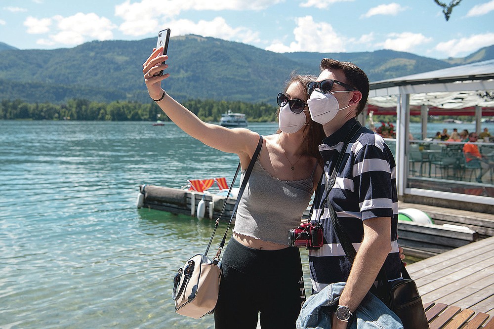 A couple make selfies at the lake side in St. Wolfgang, Austria, Monday, July 27, 2020. More than 50 corona tests in the small community of St. Wolfgang in the Salzkammergut have been positive in the past few days. Young interns in tourism companies are particularly affected, but at least one holiday guest has also been tested positive. St. Wolfgang is the most important holiday resort in Upper Austria.(AP Photo/Kerstin Joensson)