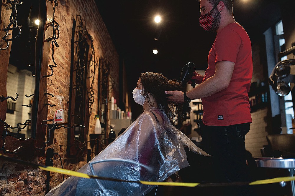 A woman, wearing a mask to protect against the spread of coronavirus, gets her hair styled in a hairdresser shop in downtown Brussels, Monday, July 27, 2020. Belgian Prime Minister Sophie Wilmes unveiled Monday a new set of drastic social distancing measures aimed at avoiding a new general lockdown amid a surge of COVID-19 infections. (AP Photo/Francisco Seco)