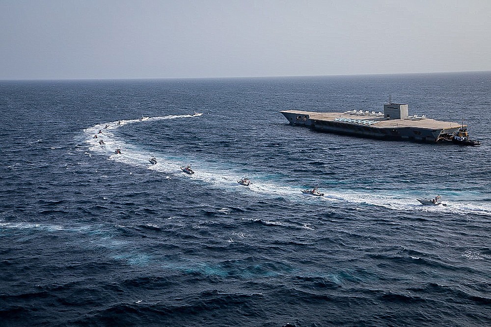 In this photo released Tuesday, July 28, 2020, by Sepahnews, Revolutionary Guard's speed boats circle around a replica aircraft carrier during a military exercise. Iran's paramilitary Revolutionary Guard has fired a missile from a helicopter targeting the mock-up aircraft carrier in the strategic Strait of Hormuz according to footage aired on state television on Tuesday. Iranian commandos also fast-roped down from a helicopter onto the replica in the footage from the exercise called "Great Prophet 14." The drill appears aimed at threatening the U.S. amid tensions between Tehran and Washington. (Sepahnews via AP)