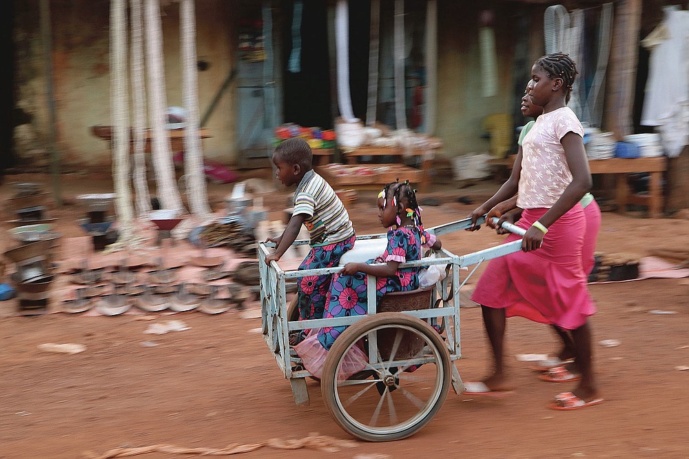 Girls push children in a cart near the market in the town of Hounde, Tuy Province, in southwestern Burkina Faso on Thursday, June 11, 2020. (AP Photo/Sam Mednick)