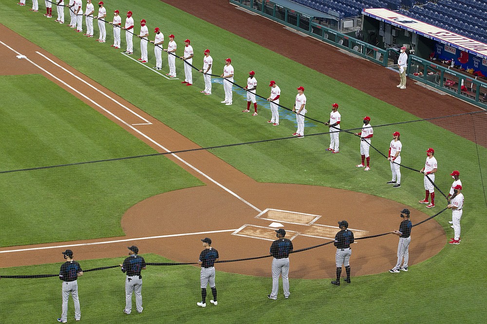 The Philadelphia Phillies, top, and the Miami Marlins hold a black ribbon in honor of the Black Lives Matter movement and in memory of George Floyd, before a baseball game Friday, July 24, 2020, in Philadelphia. Major League Baseball has already postponed a second scheduled game between Miami and Baltimore after more than a dozen Marlins players and staff tested positive for the coronavirus, prompting the club to lock down in Philadelphia. Commissioner Rob Manfred said the soonest the Marlins could resume their schedule is Wednesday, when they are set to play in Baltimore. (Charles Fox/The Philadelphia Inquirer via AP)