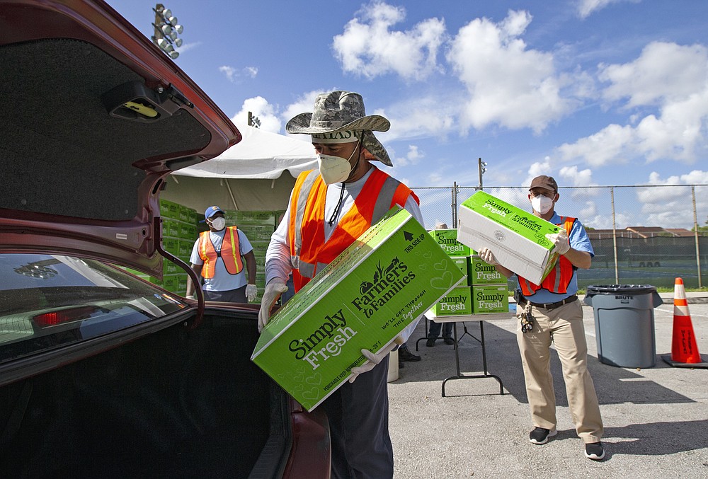 City of Hialeah employees loading up food and vegetables to hundreds of cars lined up for hours early during a drive-thru food distribution at the Goodlet Park in Hialeah, Fla., as the coronavirus pandemic continues on Wednesday, July 29, 2020. The City of Hialeah in partnership with Feeding South Florida organized the drive-thru food distribution. Food is distributed first-come, first-served while supplies last. (David Santiago/Miami Herald via AP)