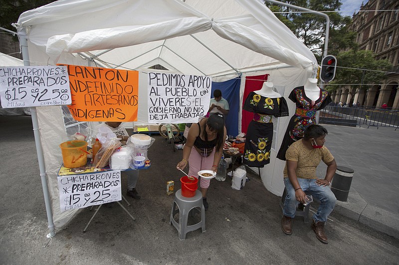 An Indigenous woman serves soup at her stall as artisans demand economic help from the government after their livelihood was severely affected by the new coronavirus lockdown, in Mexico City's main square, the Zocalo, Tuesday, July 28, 2020. With the country facing a deep economic recession, Mexican President Andres Manuel Lopez Obrador has pushed to reopen the economy quickly even as COVID-19 infections and deaths continue to rise. (AP Photo/Fernando Llano)