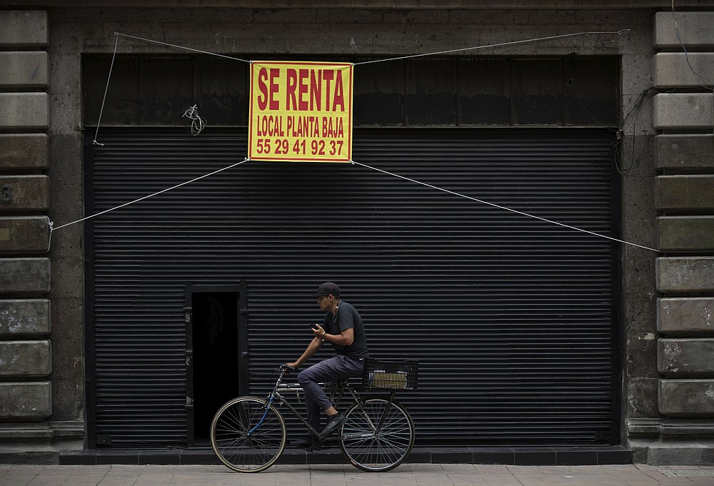 A man rides his bike past a shuttered local that is being offered for rent in downtown Mexico City, Tuesday, July 28, 2020. With the country facing a deep economic recession, Mexican President Andres Manuel Lopez Obrador has pushed to reopen the economy quickly even as COVID-19 infections and deaths continue to rise. (AP Photo/Fernando Llano)
