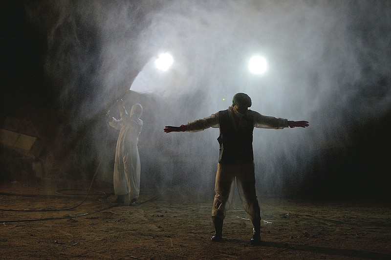A member of the Shiite Imam Ali brigades militia disinfects his colleague during funerals of coronavirus victims at Wadi al-Salam cemetery near Najaf, Iraq, Sunday, July 19, 2020. A special burial ground near the Wadi al-Salam cemetery has been created specifically for COVID-19 victims since rejections of such burials have continued in Baghdad cemeteries and elsewhere in Iraq. (AP Photo/Anmar Khalil)