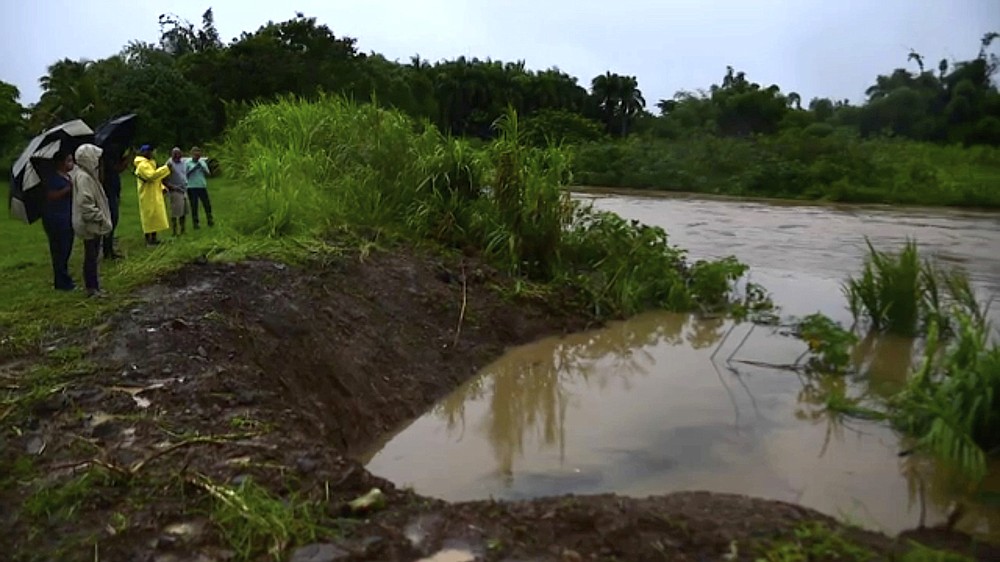 In this image made from video, people look at level of Canovanas river following heavy rain caused by the storm in Alto Trujillo, Puerto Rico, Thursday, July 30, 2020. Tropical Storm Isaias knocked out power and caused flooding and small landslides across Puerto Rico and the Dominican Republic on Thursday as forecasters predicted it would strengthen into a hurricane while moving toward the Bahamas and U.S. East Coast.(AP Photo)