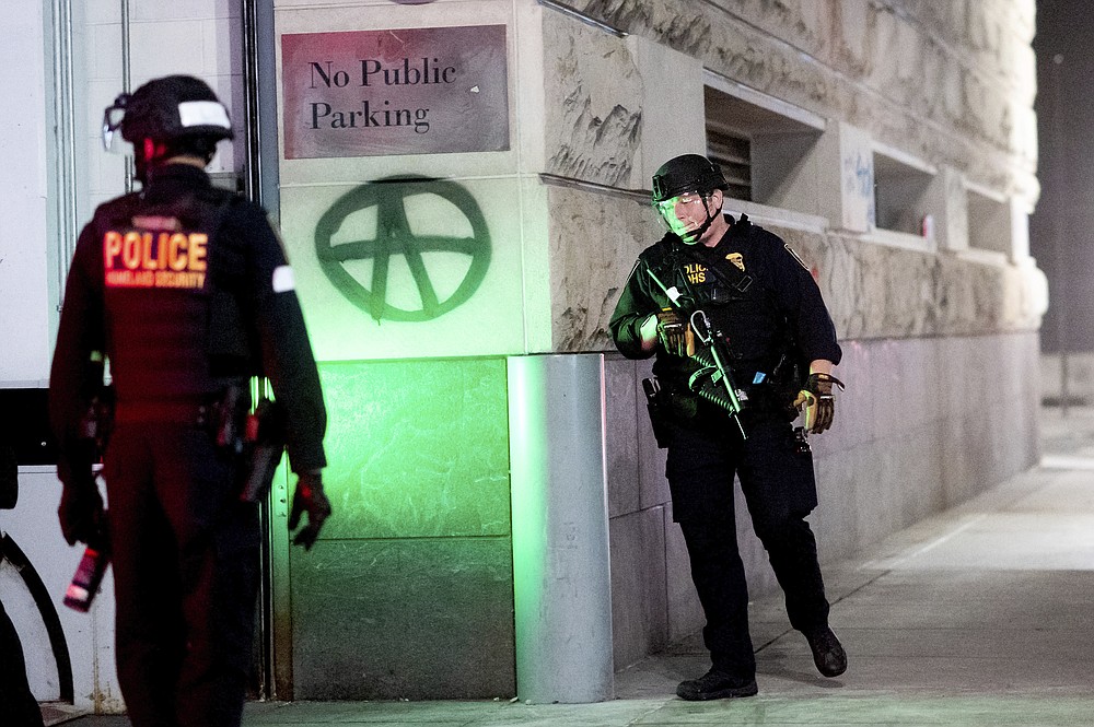 Department of Homeland Security officers guard a back entrance to the the Mark O. Hatfield United States Courthouse on Saturday, Aug. 1, 2020, in Portland, Ore. Following an agreement between Democratic Gov. Kate Brown and the Trump administration to reduce federal officers in the city, the night's protest remained largely peaceful without major confrontations between demonstrators and officers. (AP Photo/Noah Berger)