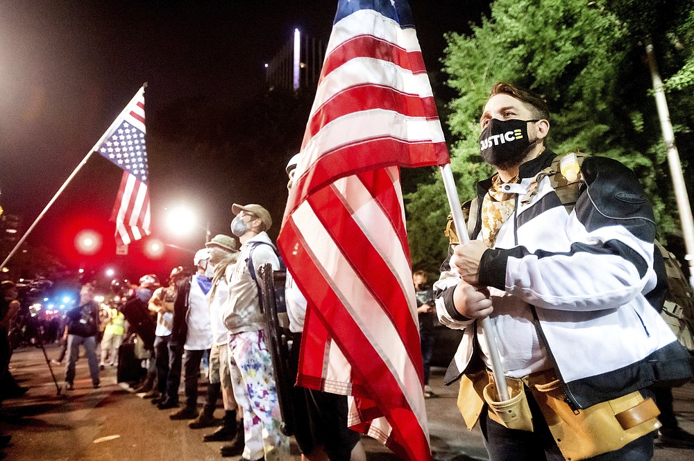 Navy veteran Adam Winther holds a flag while forming a "Wall of Vets" during a Black Lives Matter protest at the Mark O. Hatfield United States Courthouse on Friday, July 31, 2020, in Portland, Ore. Following an agreement between Democratic Gov. Kate Brown and the Trump administration to reduce federal officers in the city, nightly protests remained largely peaceful without major confrontations between demonstrators and officers. (AP Photo/Noah Berger)