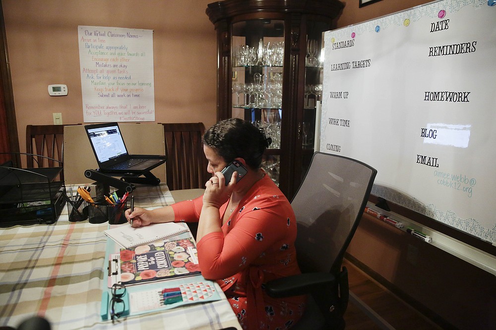 Aimee Rodriguez Webb works on her computer reading emails at her dinning room table that she set up as a virtual classroom for a Cobb County school, on Tuesday, July 28, 2020, in Marietta, Ga. After a rocky transition to distance learning last spring, Webb is determined to do better this fall. She bought a dry-erase board and a special camera to display worksheets, and she set up her dining room to broadcast school lessons. (AP Photo/Brynn Anderson)