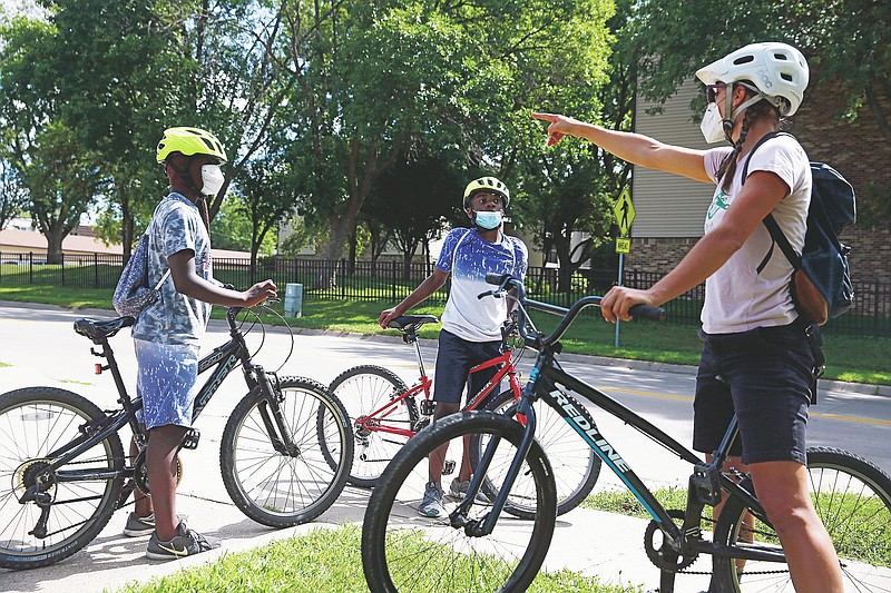 Junior Tsimba, 13, left, and Bernoli Luvandu, 11, discuss where to ride with Audrey Wiedemeier, Executive director of the Iowa City Bike Library, during Bike Club, a bike education program offered by the bike library at the Broadway Neighborhood Center in Iowa City, Iowa, on Wednesday, July 22, 2020. This summer's program has been modified due to coronavirus concerns, with smaller group sizes, disinfection of bikes and frequent sanitation by staff, and masks for participants and staff. (Liz Martin/The Gazette via AP)
