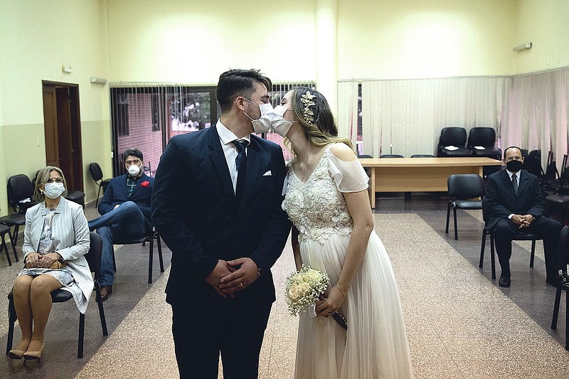FILE - Groom Raul Benitez and bride Jenny Bonet wear protective face masks as they kiss during their wedding ceremony at the Civil Registry office, in Asuncion, Paraguay, on June 13, 2020. Now that weddings have slowly cranked up under a patchwork of ever-shifting restrictions, horror stories from vendors are rolling in. Many are desperate to work after the coronavirus put an abrupt end to their incomes and feel compelled to put on their masks, grab their cameras and hope for the best. (AP Photo/Jorge Saenz, File)