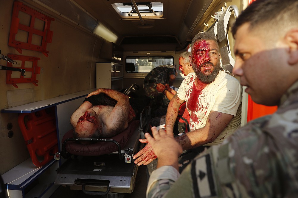 A Lebanese soldier, right, checks injured men who sit inside an umbulance at the explosion scene that hit the seaport of Beirut, Lebanon, Tuesday, Aug. 4, 2020. Massive explosions rocked downtown Beirut on Tuesday, flattening much of the port, damaging buildings and blowing out windows and doors as a giant mushroom cloud rose above the capital. (AP Photo/Hussein Malla)