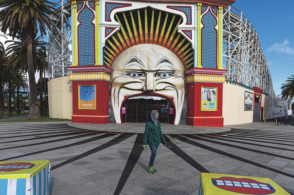 A man wearing a mask walks past Luna Park in the suburb of St Kilda during lockdown in Melbourne, Australia, Wednesday, Aug. 5, 2020. People are allowed to exercise for one hour a day within a 5-kilometer radius of their house. Victoria state, Australia's coronavirus hot spot, announced on Monday that businesses will be closed and scaled down in a bid to curb the spread of the virus. (AP Photo/Asanka Brendon Ratnayake)
