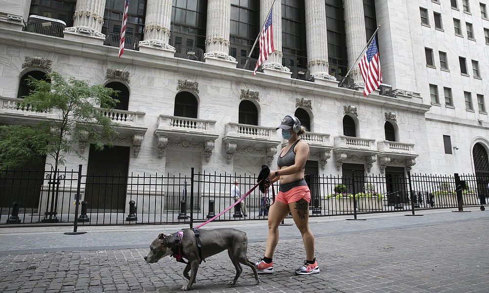 FILE - A woman wearing a mask walks her dog past the New York Stock Exchange, Tuesday, June 30, 2020. Stocks are drifting in early trading on Wall Street Thursday, Aug. 6, after a report suggested that the number of layoffs across the country is slowing, though it remains incredibly high. (AP Photo/Mark Lennihan)