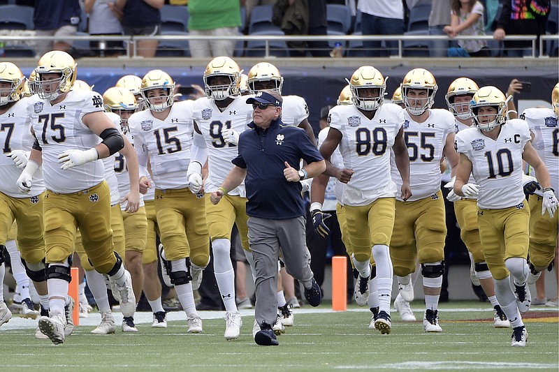 FILE - In this Dec. 28, 2019, file photo, Notre Dame head coach Brian Kelly, center, runs onto the field with his players before the Camping World Bowl NCAA college football game against Iowa State in Orlando, Fla. The Atlantic Coast Conference and Notre Dame are considering whether the Fighting Irish will give up their treasured football independence for the 2020 season play as a member of the league. (AP Photo/Phelan M. Ebenhack, File)