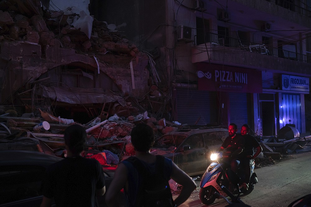 People ride past damaged buildings at a neighborhood without electricity near the scene of Tuesday's explosion that hit the seaport of Beirut, Lebanon, Friday, Aug. 7, 2020. Rescue teams were still searching the rubble of Beirut's port for bodies on Friday, nearly three days after a massive explosion sent a wave of destruction through Lebanon's capital, killing over a hundred people and wounding thousands. (AP Photo/Felipe Dana)