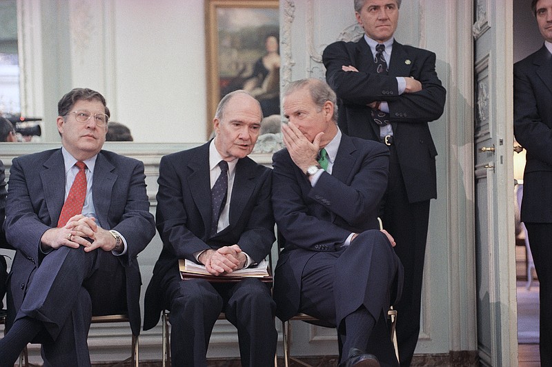 FILE - In this Nov. 21, 1990 file photo, Secretary of State James Baker whispers to National Security Advisor Brent Scowcroft during an impromptu press conference by President George H. W. Bush in Paris.  At left is White House Chief of Staff John Sununu. A longtime adviser to Presidents Gerald Ford and George H.W. Bush has died. Brent Scowcroft was 95. A spokesperson for the late President Bush says Scowcroft died Thursday of natural causes at his home in Falls Church, Virginia.(AP Photo/Scott Applewhite)