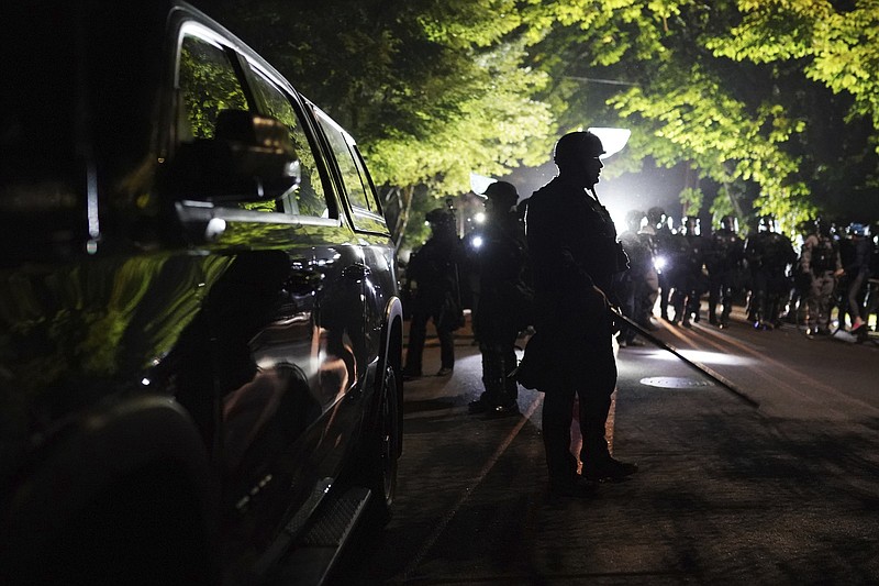 Portland police officers walk through the Laurelhurst neighborhood after dispersing protesters from the Multnomah County Sheriff's Office early in the morning on Aug. 8, 2020 in Portland, Ore. (AP Photo/Nathan Howard)