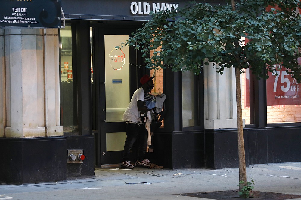 A person exits an Old Navy store in the Chicago Loop with an armful of clothing in the early morning of Monday, Aug. 10, 2020 in Chicago. Hundreds of people smashed windows, stole from stores and clashed with police early Monday in Chicago's Magnificent Mile shopping district and other parts of the city's downtown. (Jose M. Osorio /Chicago Tribune via AP)