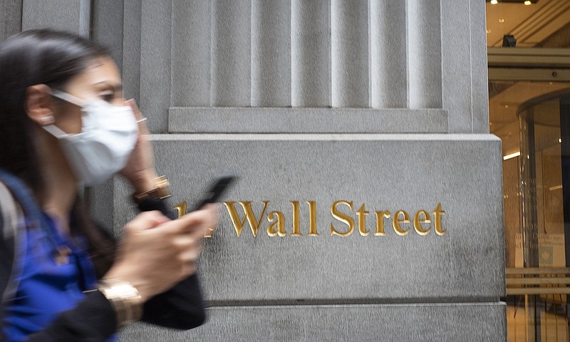 FILE - In this June 30, 2020 file photo, a woman wearing a mask passes a sign for Wall Street during the coronavirus pandemic.   Stocks are opening higher on Wall Street, pushing the S&P 500 ever closer to the all-time high it reached back in February, before the coronavirus shutdowns slammed the economy. The index was up 0.3% in the early going Tuesday, Aug. 11.  (AP Photo/Mark Lennihan, File)