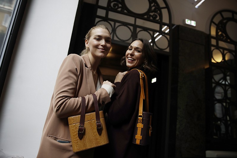 FILE - In this Feb. 24, 2019 file photo, model Arizona Muse, left, is flanked by designer and Officina del Poggio owner Allison Hoeltzel Savini as they present a creation of the Officina del Poggio women's Fall-Winter 2019-2020 collection, in Milan, Italy. The United States’ fumbling response to the pandemic is casting doubt on its economic prospects and making it one of the chief risks that could undermine the rebound. Officina del Poggio sells 60% its vintage motorcycle-inspired satchels to U.S. customers. (AP Photo/Luca Bruno, file)