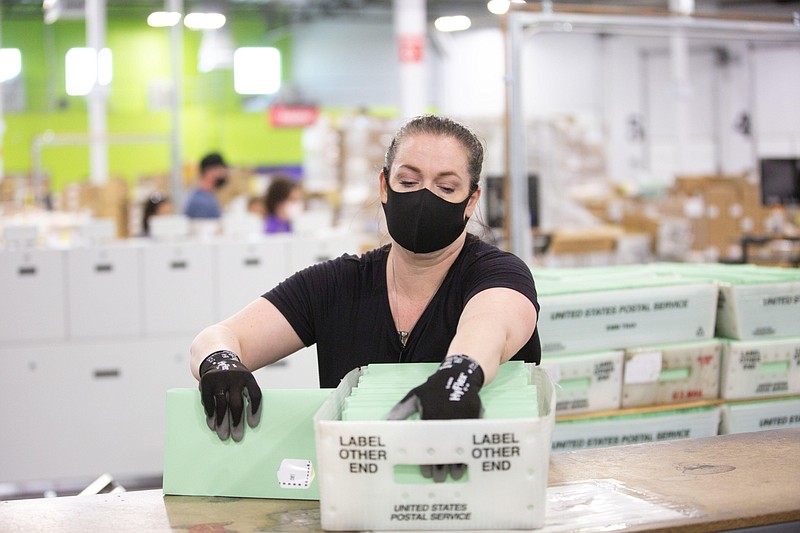 A worker wearing a protective mask places enveloped ballots into a postal service bin at the Runbeck Election Services facility in Phoenix on June 23, 2020. MUST CREDIT: Bloomberg photo by Caitlin O'Hara.