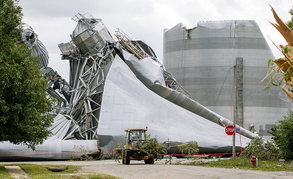 Iowa Department of Transportation workers help with tree debris removal as grain bins from the Archer Daniels Midland facility are seen severely damaged in Keystone, Iowa, on Wednesday, Aug. 12, 2020. A storm slammed the Midwest with straight line winds of up to 100 miles per hour on Monday, gaining strength as it plowed through Iowa farm fields, flattening corn and bursting grain bins still filled with tens of millions of bushels of last year’s harvest. (Jim Slosiarek/The Gazette via AP)