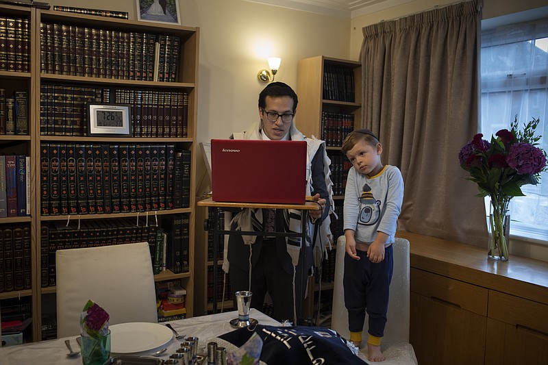 As his 3-year-old son Tzvi looks on, Rabbi Mordechai Chalk leads a service for his congregation via a teleconferencing app from his home in London on June 19 just before sunset. Taking services online-only has been particularly challenging for the Orthodox Jewish community, members of which are proscribed from using electronics on Shabbat, their day of rest.
(AP/Elizabeth Dalziel)