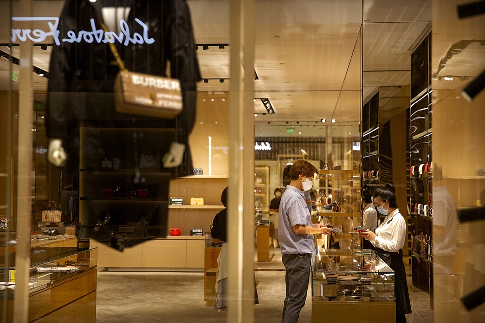 An employee wearing a face mask to protect against the coronavirus helps a man make a purchase at a store in a shopping mall in Beijing, Friday, Aug. 14, 2020. China's factory output rose just under 5% last month from a year earlier while retail sales fell slightly, suggesting the country's recovery from the coronavirus pandemic remains muted. (AP Photo/Mark Schiefelbein)