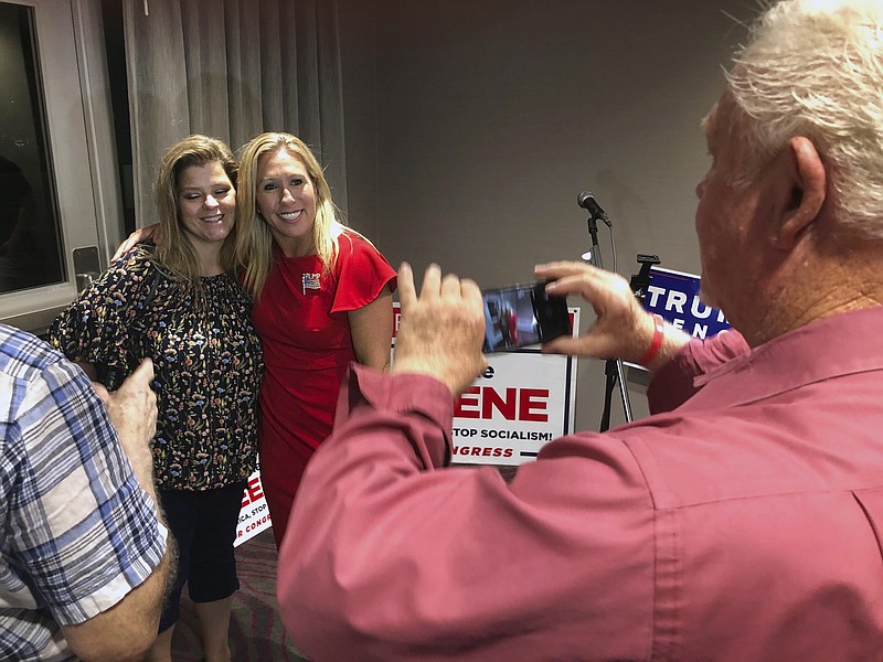 Supporters take photos with construction executive Marjorie Taylor Greene, background right, late Tuesday, Aug. 11, 2020, in Rome, Ga. Greene, criticized for promoting racist videos and adamantly supporting the far-right QAnon conspiracy theory, won the GOP nomination for northwest Georgia's 14th Congressional District. (AP Photo/Mike Stewart)
