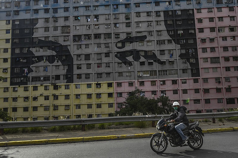 A biker wearing a protective face mask rides past a mural depicts "Chavez's eyes" a design based on the eyes of the late Venezuelan President Hugo Chavez at the 23 de Enero neighborhood of Caracas, Venezuela, Thursday, July 30, 2020, amid the new coronavirus pandemic. (AP Photo/Matias Delacroix)