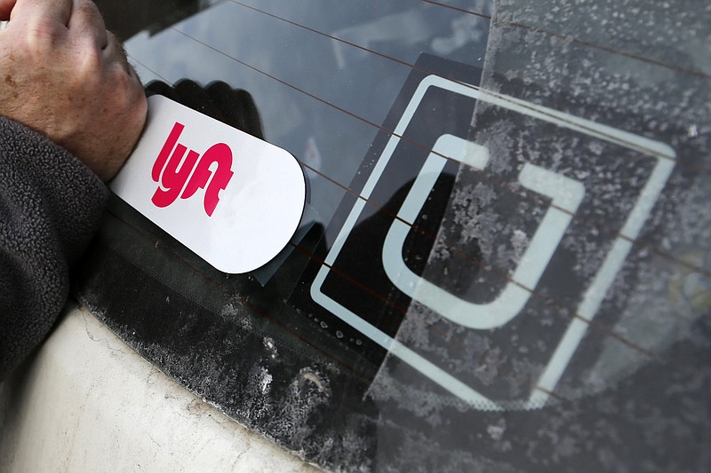 FILE- In this Jan. 31, 2018, file photo, a Lyft logo is installed on a Lyft driver's car next to an Uber sticker in Pittsburgh.  Ride-hailing giants Uber and Lyft on Thursday, Aug. 20, 2020, are saying they will shut down their California operations if a new law goes into effect overnight which would force both companies to classify their drivers as employees.    (AP Photo/Gene J. Puskar, File)