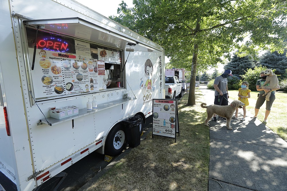 Bobby Price, left, and Catherine Vogt, right, stand with Catherine's daughter Avery, 8, and their dogs as they wait to order from the YS Street Food food truck, Monday, Aug. 10, 2020, near the suburb of Lynnwood, Wash., north of Seattle. Long seen as a feature of city living, food trucks are now finding customers in the suburbs during the coronavirus pandemic as people are working and spending most of their time at home. (AP Photo/Ted S. Warren)