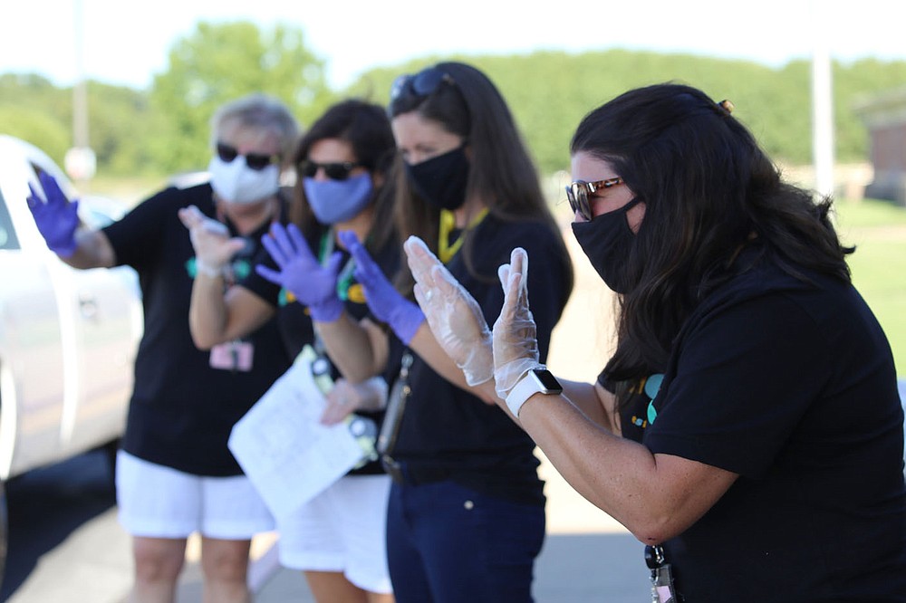 Art teacher Olivia Slone, right, and other teachers at Tucker Elementary School in Lowell wave to incoming students and their families on Thursday during a back-to-school drive-thru event to deliver school supplies and meet each other. Staff and students will wear masks when school begins Monday, with unmasked outdoor breaks throughout the day. It'll be a challenge to keep young kids masked, Slone said, but "we'll do our best." Check out nwaonline.com/200823Daily/ for a photo gallery.
(NWA Democrat-Gazette/Dan Holtmeyer)