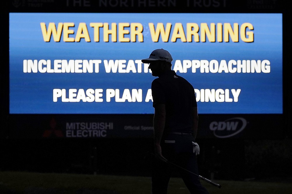 Dustin Johnson is silhouetted in the glow of a weather warning sign on the 17th hole during the final round of the Northern Trust golf tournament at TPC Boston, Sunday, Aug. 23, 2020, in Norton, Mass. (AP Photo/Charles Krupa)