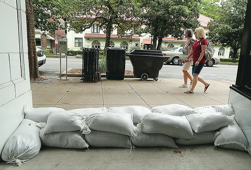 Pedestrians stroll past the sandbagged entrance to The Avenue restarant in The Waters Hotel in the 300 block of Central Ave., Tuesday. Photo by Richard Rasmussen