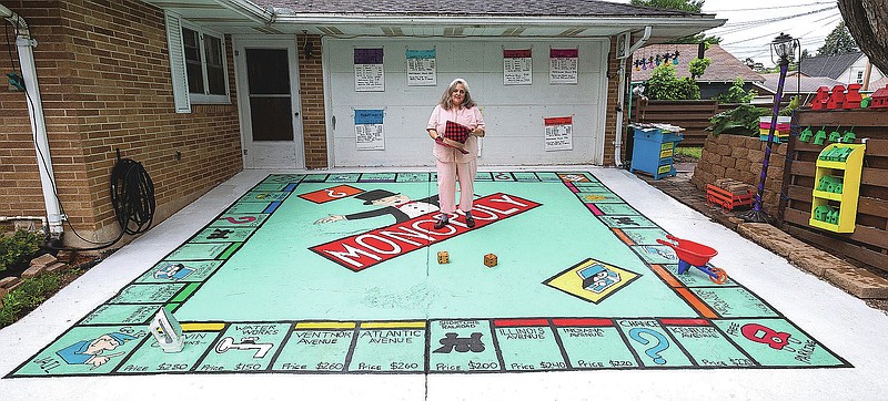 Diana Brennan stands in the center of the gigantic Monopoly game set she made in the driveway of her home IN Virginia, Minn., Thursday, July 16, 2020, while holding the top hat which inspired her to start the project. (Mark Sauer/The Mesabi Daily News via AP)