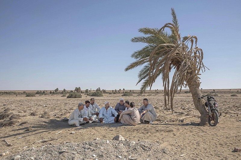 FILE - In this Wednesday, Aug. 5, 2020 file photo, Egyptian farmer Makhluf Abu Kassem, 55, center, sits with farmers under the shade of a dried up palm tree surrounded by barren wasteland that was once fertile and green, in Second Village, Qouta town, Fayoum, Egypt. The State Department said Wednesday, Sept. 2, 2020 that on the guidance of President Donald Trump the U.S. is suspending some aid to Ethiopia over the "lack of progress" in talks with Egypt and Sudan over a massive, disputed dam project which Egypt has called an existential threat and worries will reduce the country's share of Nile waters. (AP Photo/Nariman El-Mofty, File)