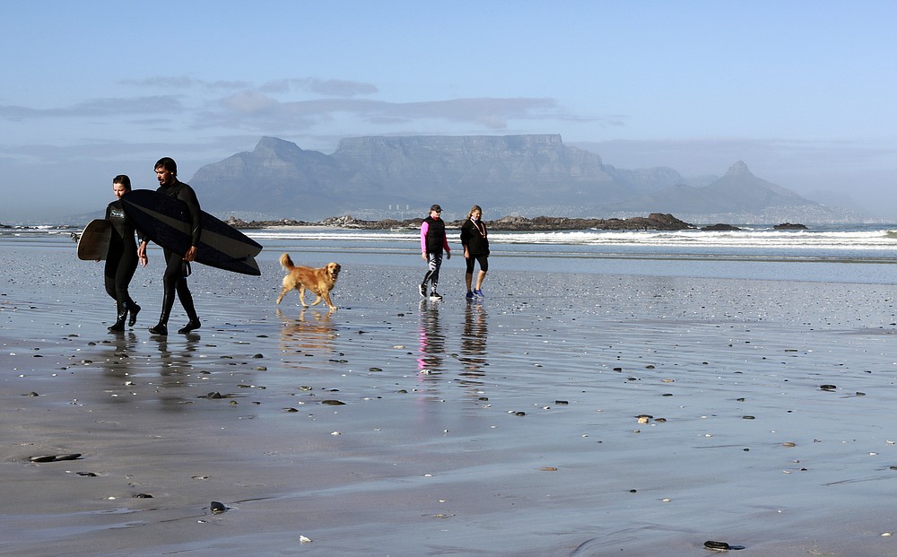 People walk on a beach, with Table Mountain in the background, in Cape Town, South Africa, Wednesday Aug. 19, 2020. Africa's tourism sector is struggling to cope with the drop in international travel caused by the COVID-19 pandemic. The World Travel and Tourism Council estimates the drop in travel caused by the COVID-19 pandemic will see Africa lose between $53 billion and $120 billion in contributions to its GDP in 2020. ( AP Photo/Nardus Engelbrecht)